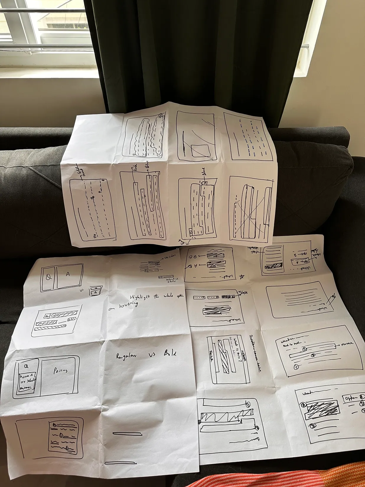Paper wireframes sketched across folded sheets on a couch
